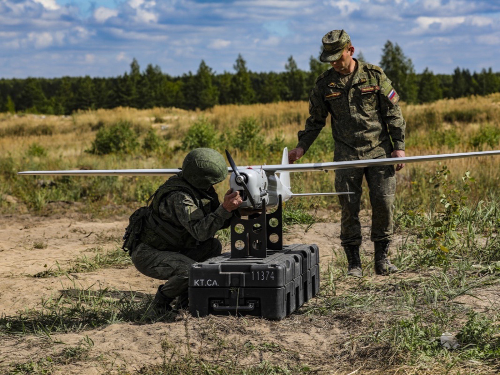 Два военнослужащих у беспилотника «Орлан-10» на стойке на транспортном кейсе, один осматривает аппарат, второй стоит рядом